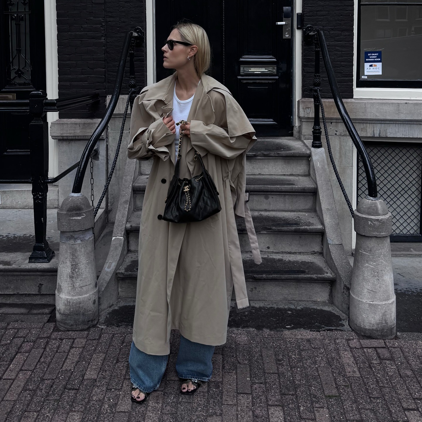 @lindatol_ wearing a white tee, trench coat, and wide-leg jeans.