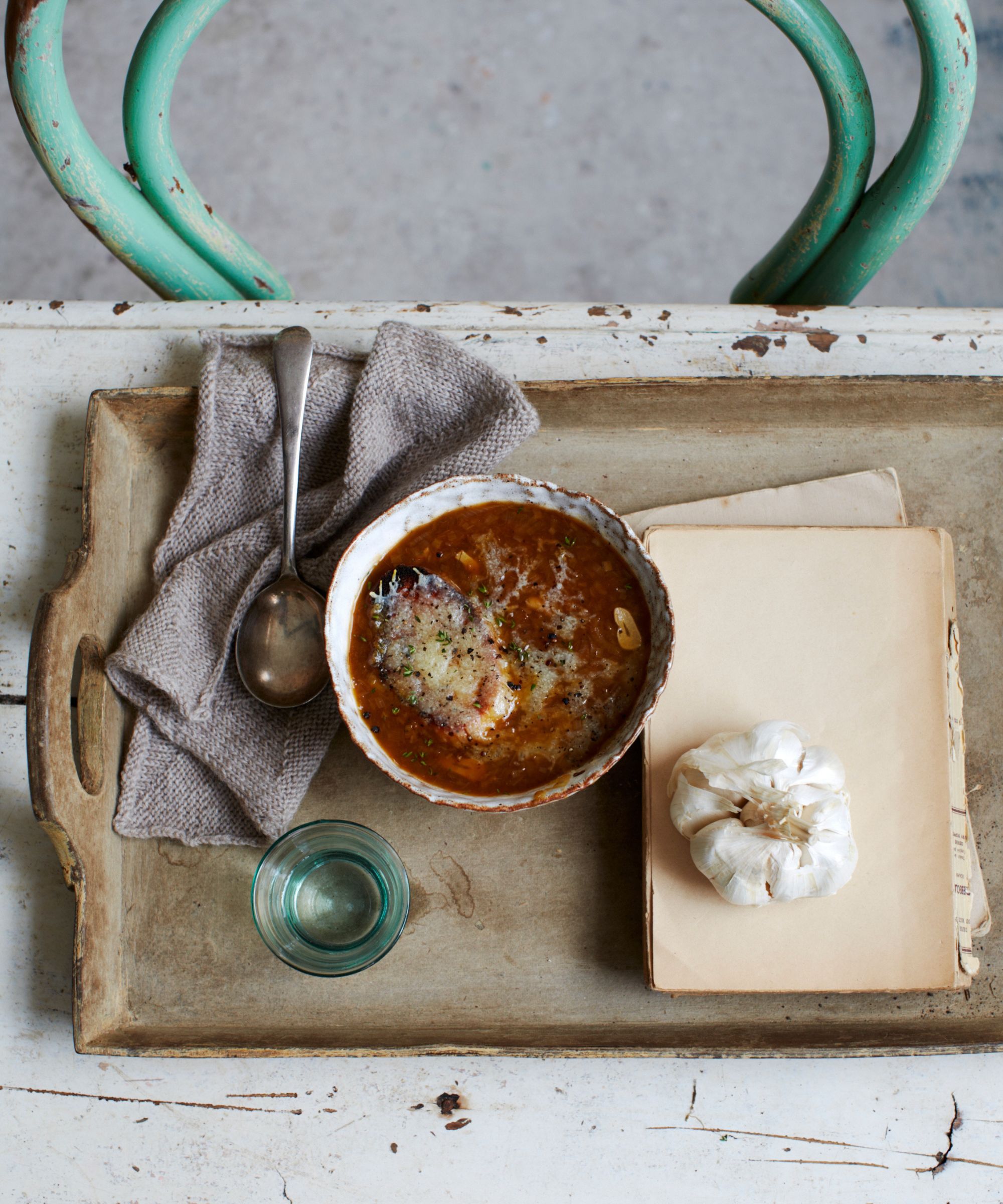 Bowl of onion soup on a tray next to a bulb of garlic, napkin and glass of water