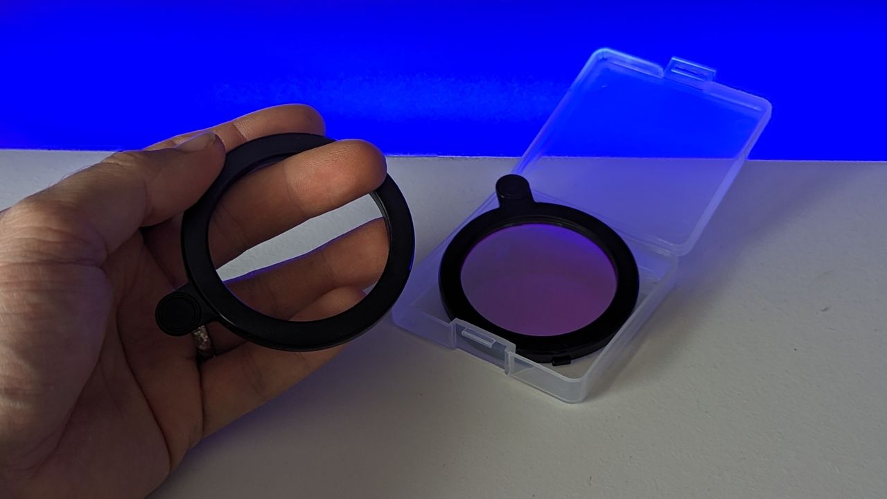 Vaonis Vespera II's light pollution filter and its box on a white table in front of a black background with a blue light shining