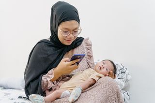 mum looking at phone while holding her baby in her lap