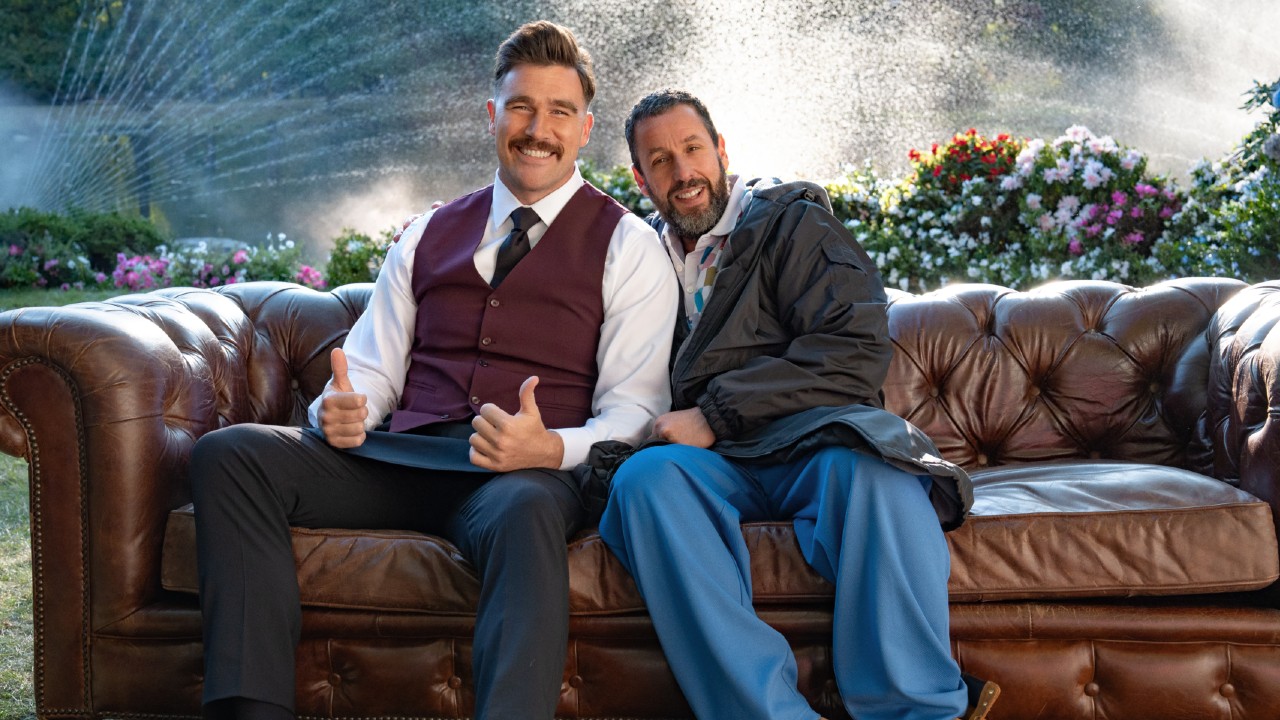 (L to R) Travis Kelce as The Waiter giving two thumbs up and Adam Sandler as Happy Gilmore sitting next to each other on a couth.