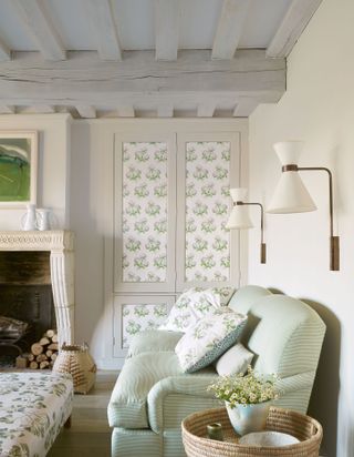 A small white living room storage idea with white painted ceiling beams, green sofa ad floral-print upholstery.