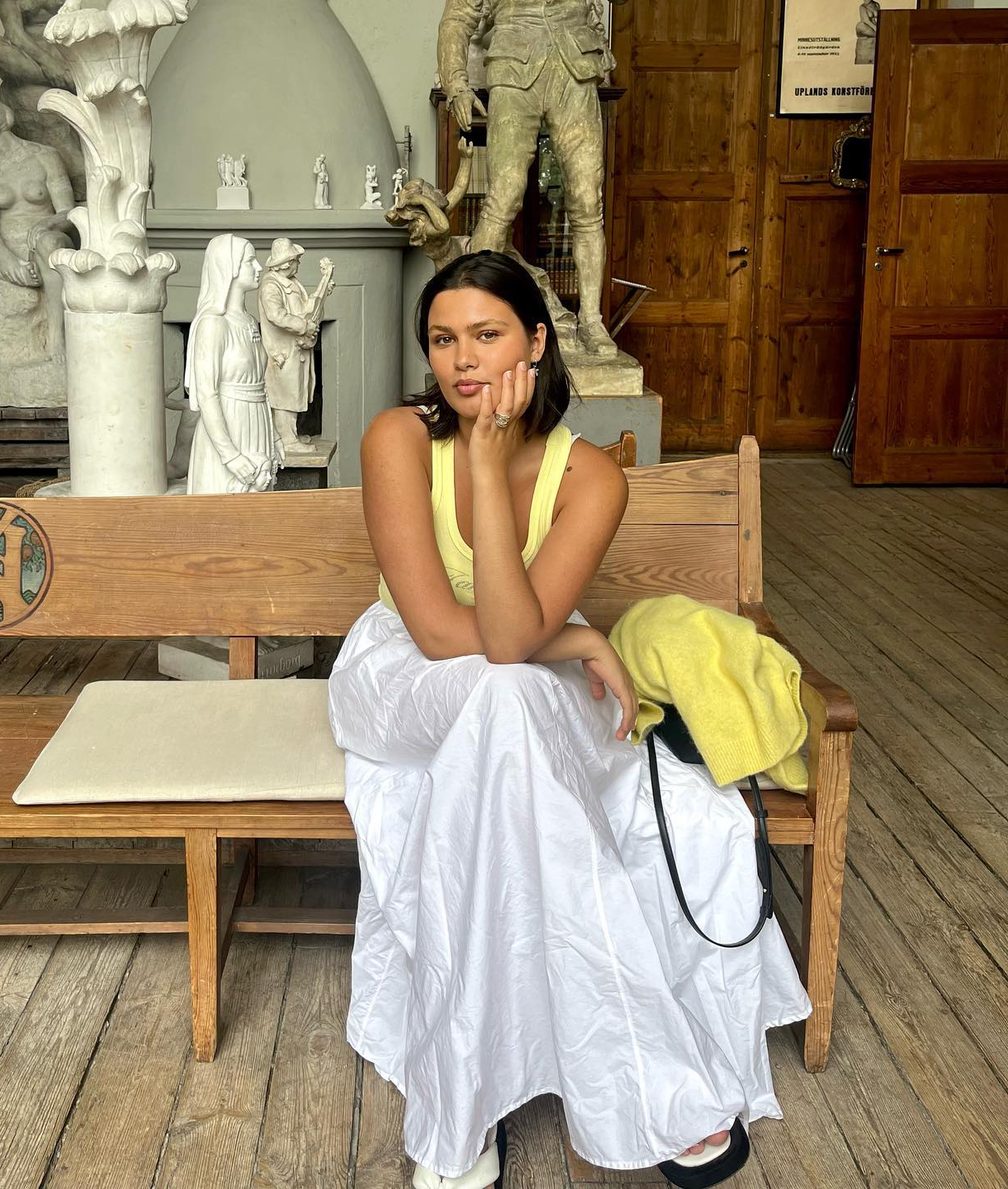 Cotton Skirt Trend: @isabellecoheen wears a white cotton skirt with a yellow top whilst sitting in an art gallery