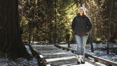 Woman walking in snowy woods looking up at a tree