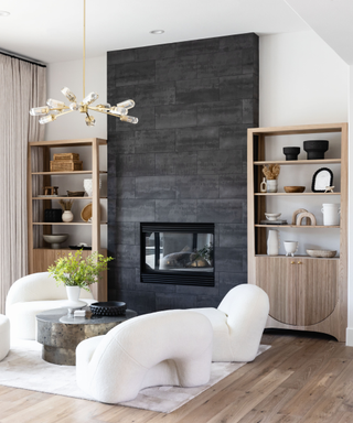 Modern living room space with white sinuous couch, wooden open shelving units and black fireplace