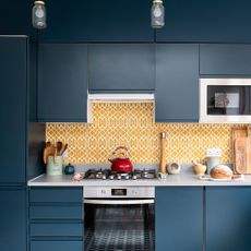 A kitchen with blue cabinets and white tiled splashback with a gas hob/oven
