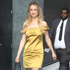 Grace van patten wears a gold satin minidress, black sheer tights, black heels, black leather bag.