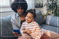 Mum with daughter sitting on sofa looking at smart phone