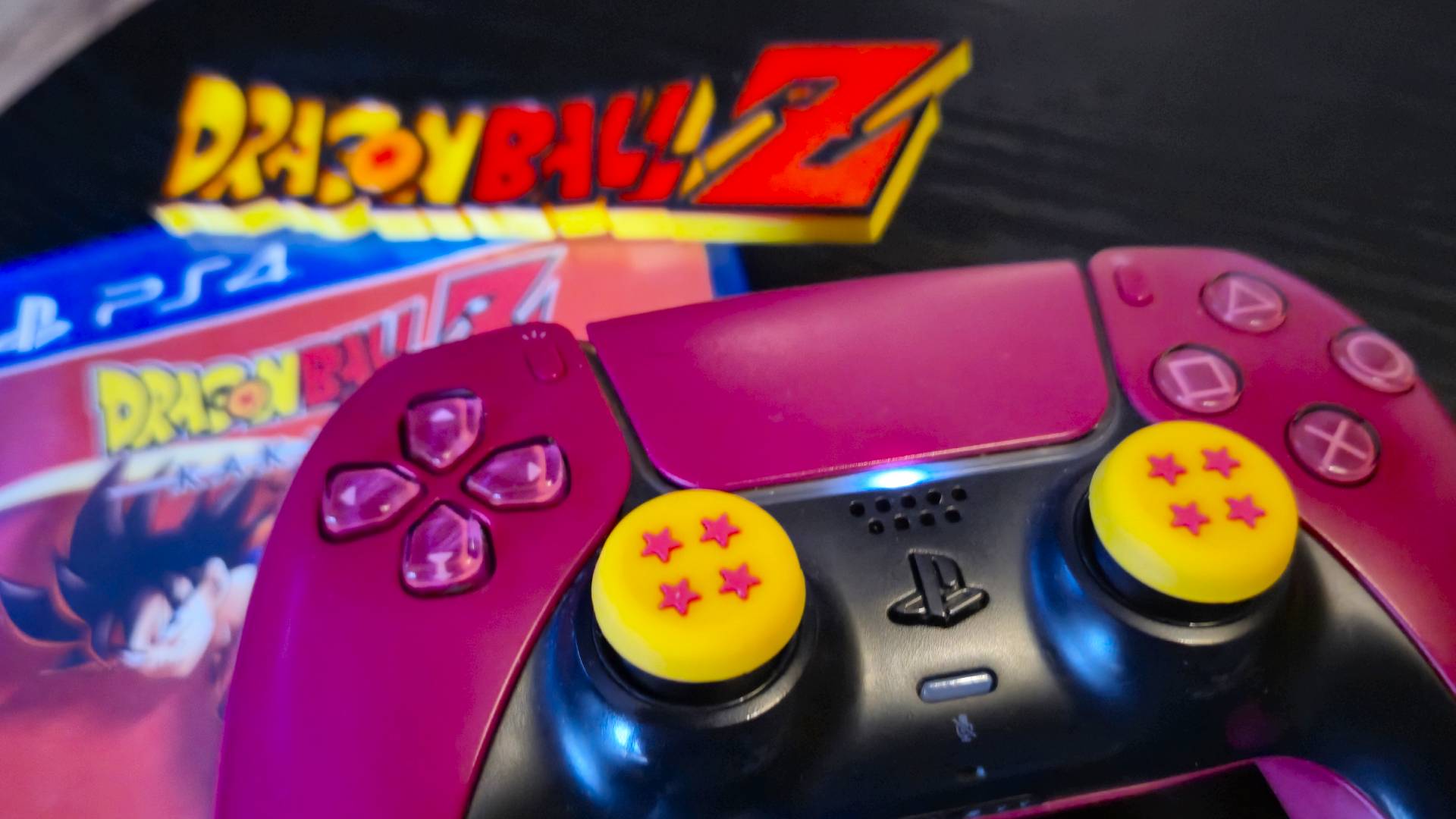 Photo by Rosalie Newcombe of the Dragon Ball Z thumb grips on a red PS5 DualSense controller, with a copy of a Dragon Ball PS4 game in the background.