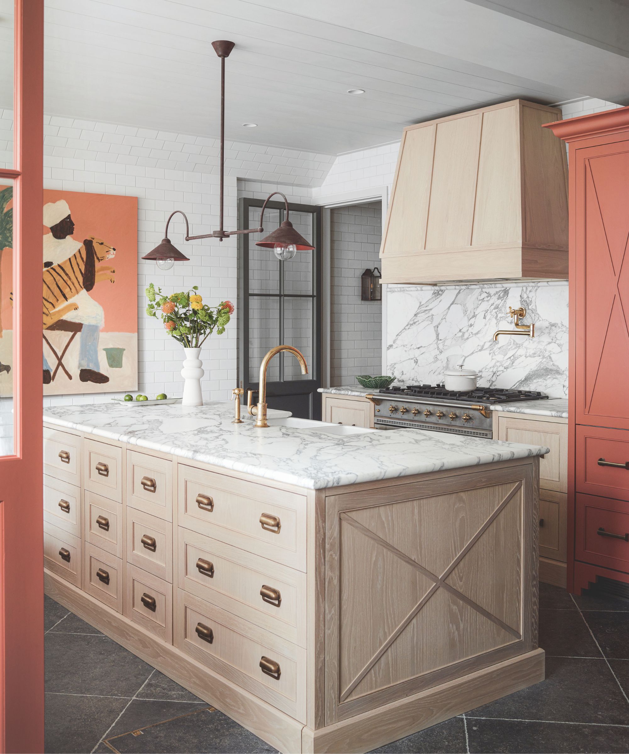 A marble, wood and terracotta kitchen with a large wooden island with marble countertop, marble backsplash, gold taps and terracotta accents on doors, cabinets and artworks.