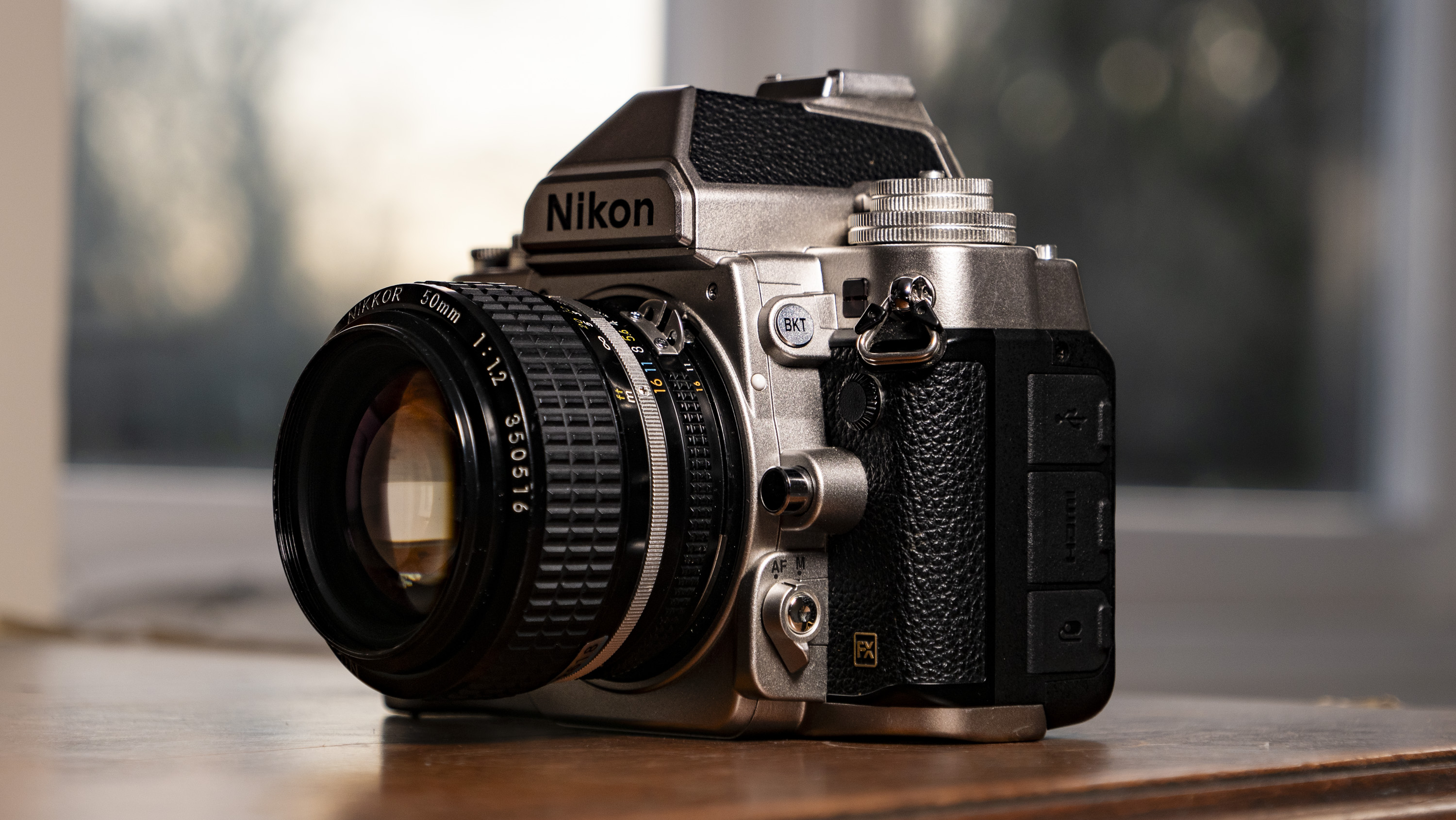 Nikon Df DSLR camera on a wooden surface by large window, with dusk light