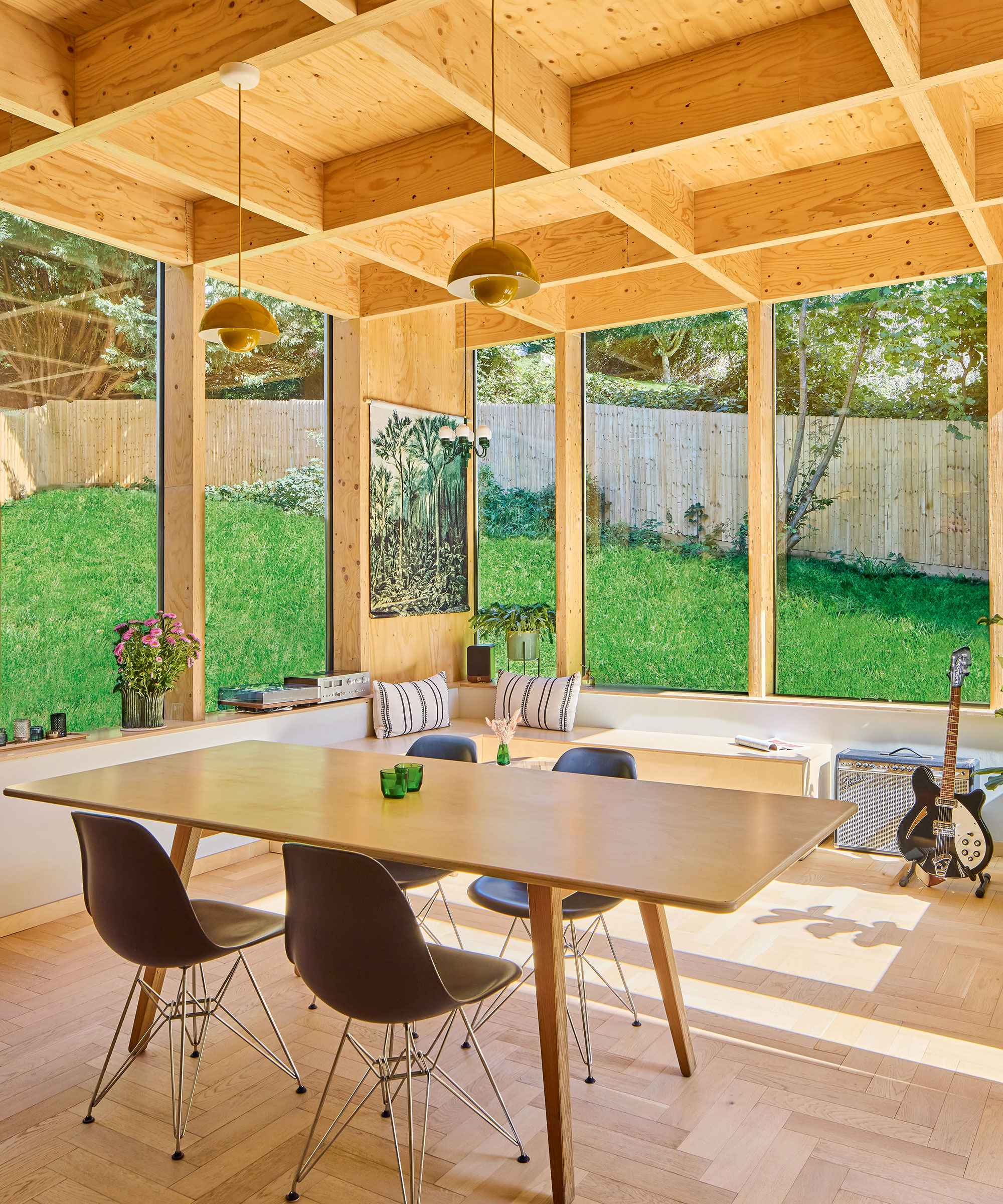 a modern timber frame extension used as a dining area with plywood interior, parquet flooring and large windows overlooking a lawned garden