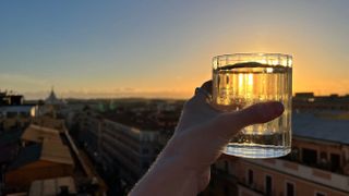 A photo of a cocktail glass with a sunset and city views in the background