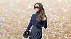 victoria beckham in a blue sweater and sunglasses playing with her hair on a gold sparkly background