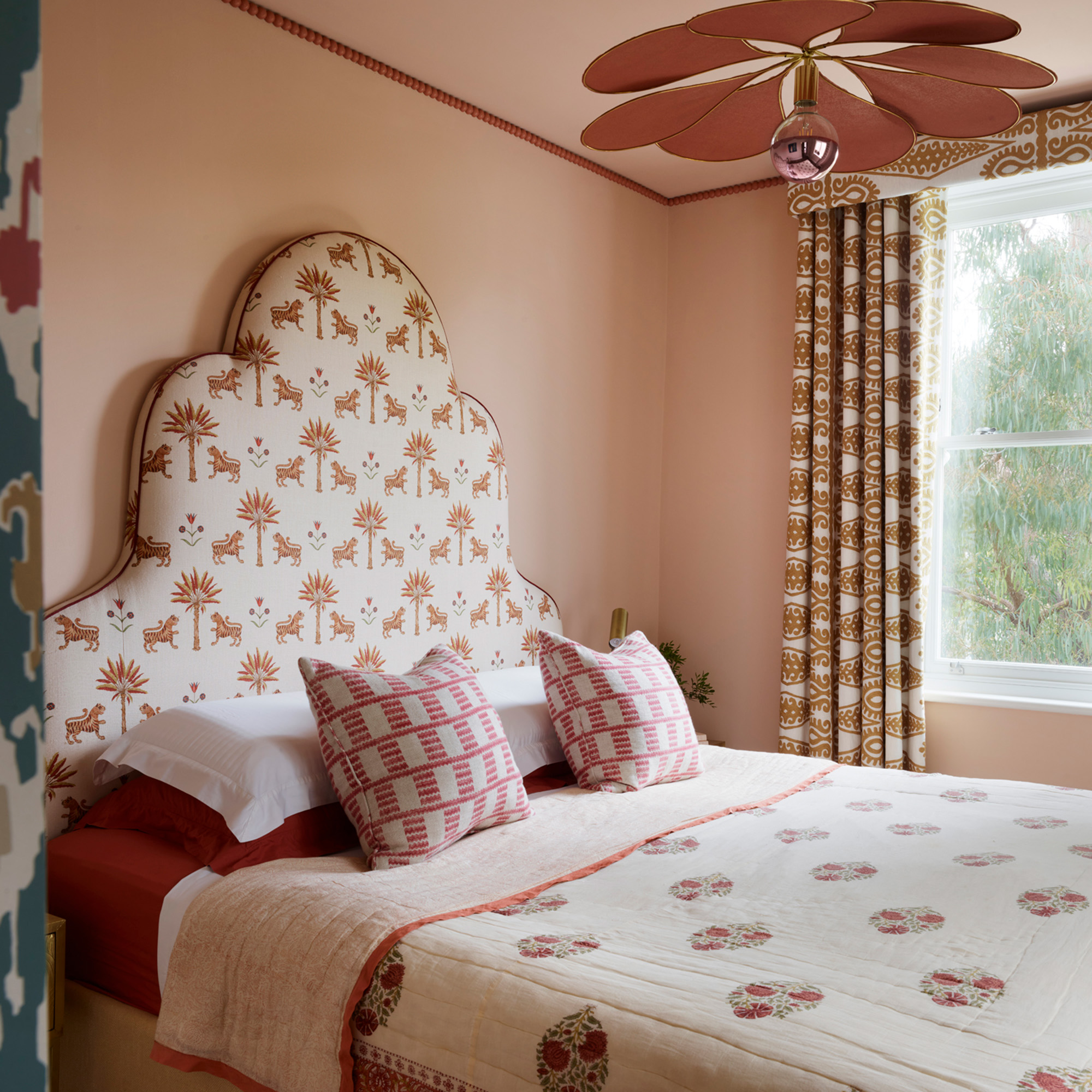 bedroom with cream patterned headboard with cream bedlinen with orange details in pale pink bedroom studio raymond