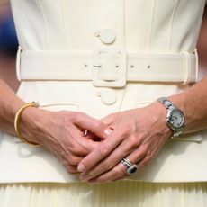 A closeup of Kate Middleton wearing a pale yellow dress, watch, bangle bracelet and stack of engagement/wedding rings