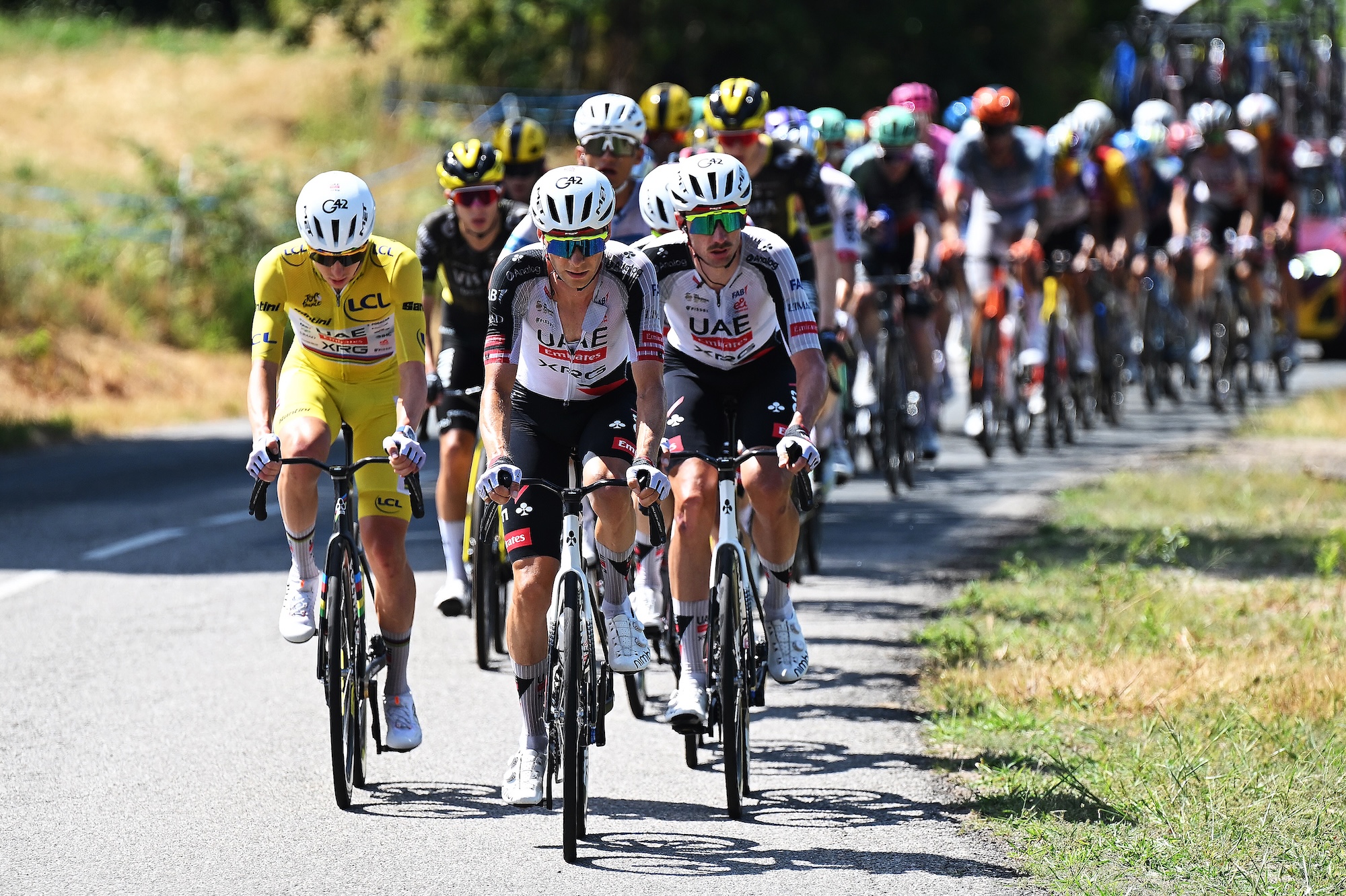 Tadej Pogacar, in the Yellow Leader Jersey, rides in the peloton on stage 12 next to UAE Team Emirates-XRG teammates Felix Grossschartner and Brandon McNulty