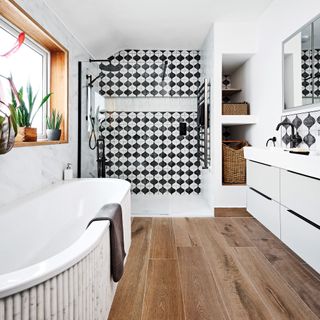 a bathroom with wood flooring, black and white patterned tiles, and marble tiled walls, with a pale grey twin vanity unit and storage baskets in a small alcove