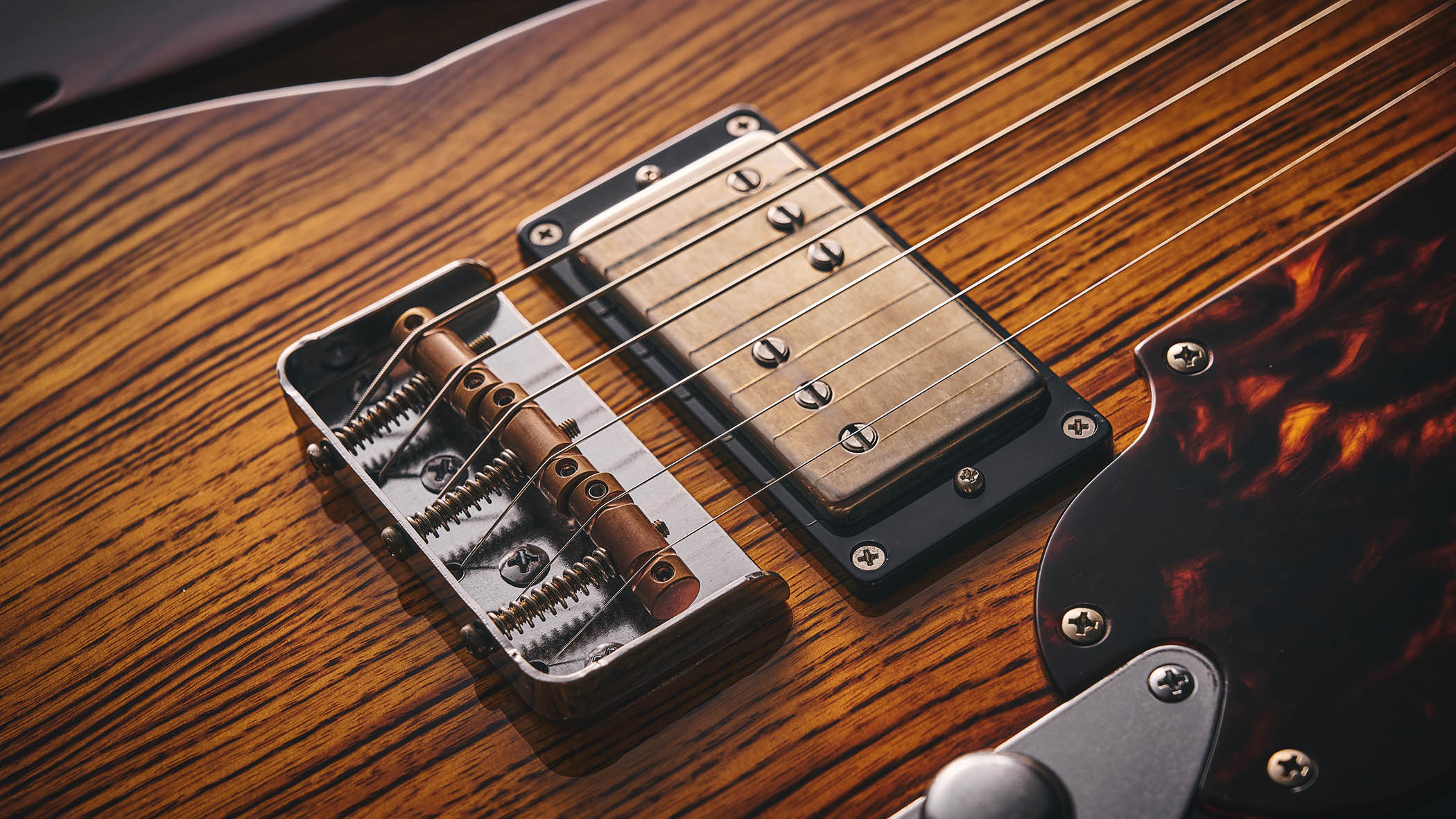 Patrick James Eggle Oz-t Cabronita Thinline; this semi-hollow T-style has a dark sunburst that reveals all the open grain, complementing the tortoiseshell pickguard, and is photographed here against a distressed floor, white and wooden backgrounds.
