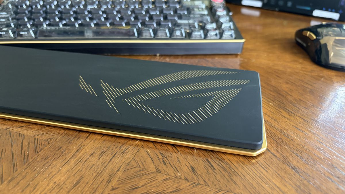 ASUS ROG black wrist rest with gold emblem on a wooden desk, next to a keyboard and mouse.