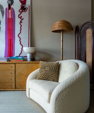 boucle chair next to a wooden sideboard filled with large art and a rattan floor lamp