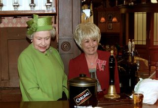 LONDON, UNITED KINGDOM - NOVEMBER 28: The Queen Visiting The Set Of The " Eastenders " Television Show During A Broadcasting Theme Day. Meeting Barbara Windsor ( Who Plays Barmaid And Pub Manager Peggy Mitchell ). The Queen Is Behind The Bar In The Old Vic Pub. (Photo by Tim Graham Picture Library/Getty Images)