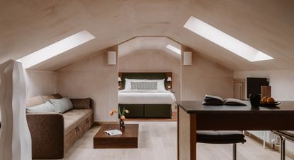 A loft conversion with pale wooden floors, argilla walls, and elegant, minimalist furniture in wood, white paper, and velvety beige fabric.