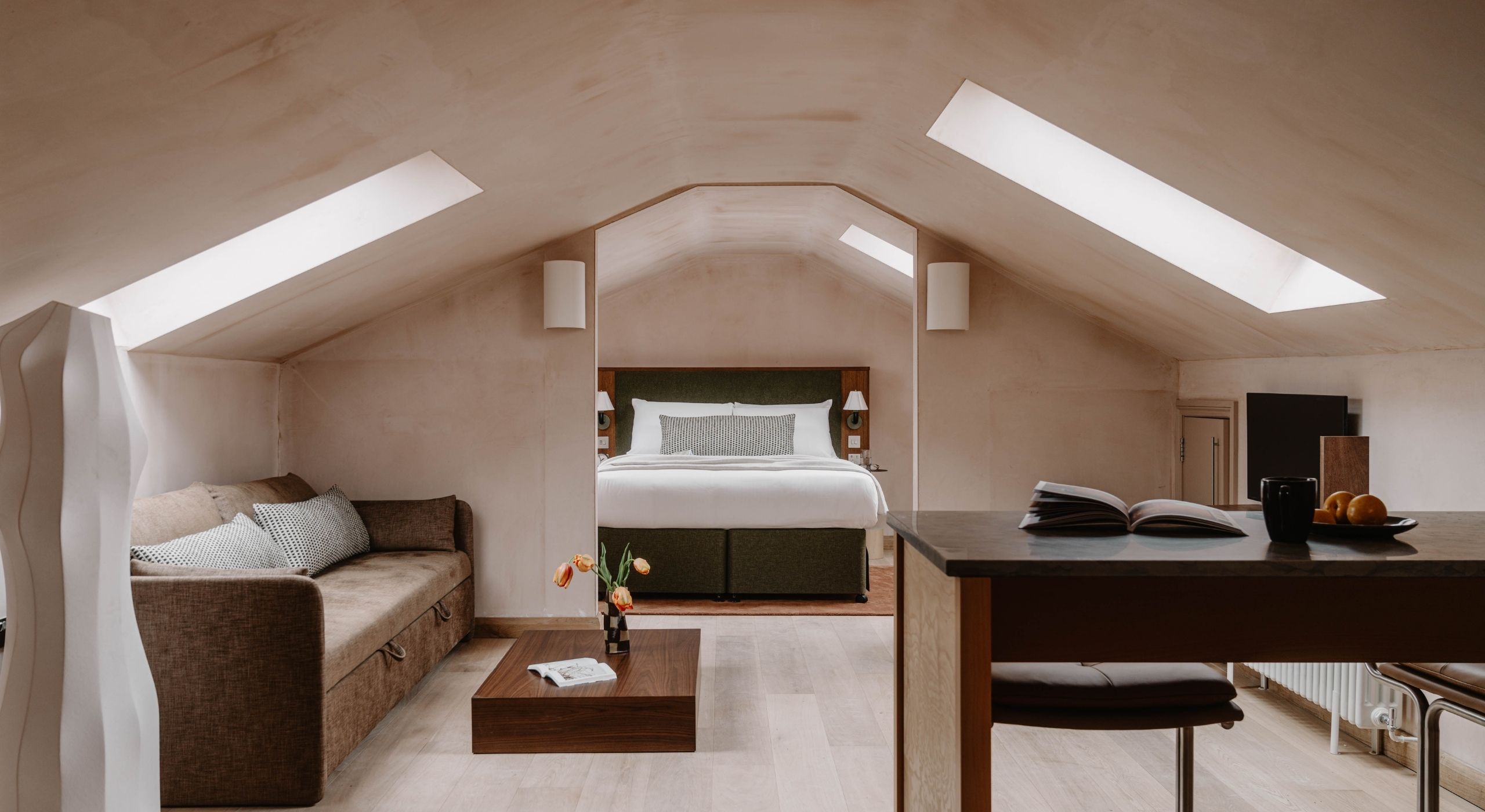 A loft conversion with pale wooden floors, argilla walls, and elegant, minimalist furniture in wood, white paper, and velvety beige fabric.