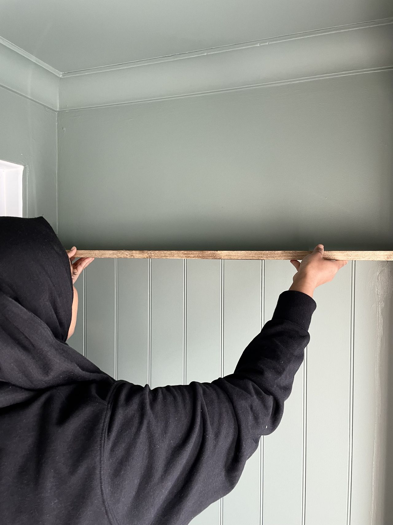 A woman positions a floating shelf into place above wood panelled walls