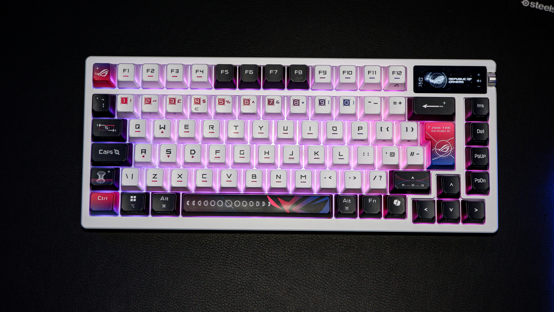 An Asus ROG Azoth X gaming keyboard on a desk with wrist rest and lighting enabled.