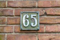 the number 65 on a metal tile against a brick wall