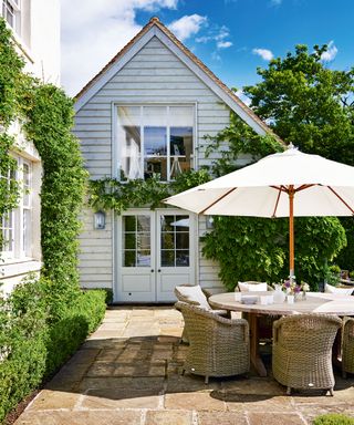 A patio area with a round dining table and parasol in front of a house