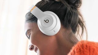 Hero image for the Beats Studio Pro will be better than the AirPods Max feature showing Beats Studio headphones worn by a female model wearing an orange pullover