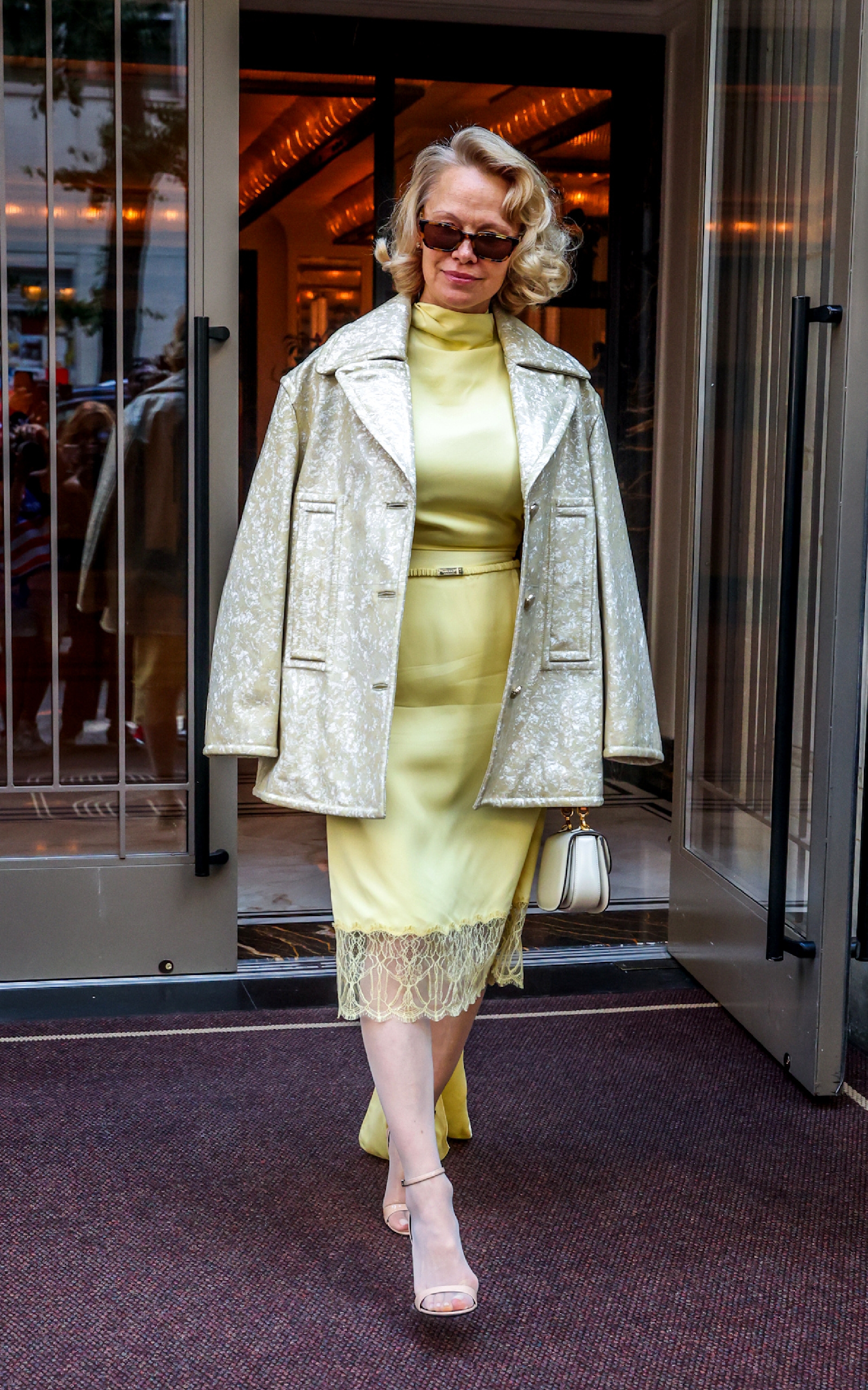 Pamela Anderson steps outside wearing tights with open-toe sandals and a knee-length skirt.