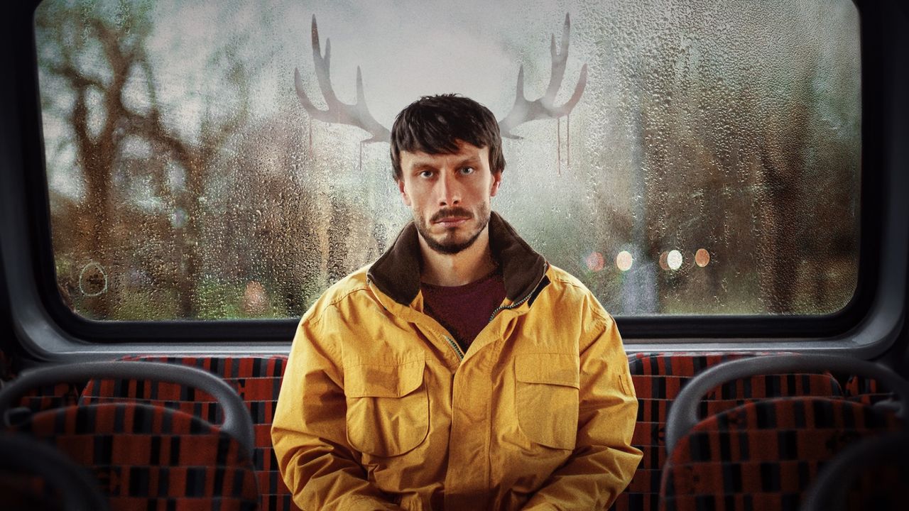 Richard Gadd as Donny Dunn, sitting at the back of the bus with reindeer antlers reflected in the window, in a promo image from the show &#039;baby reindeer&#039;