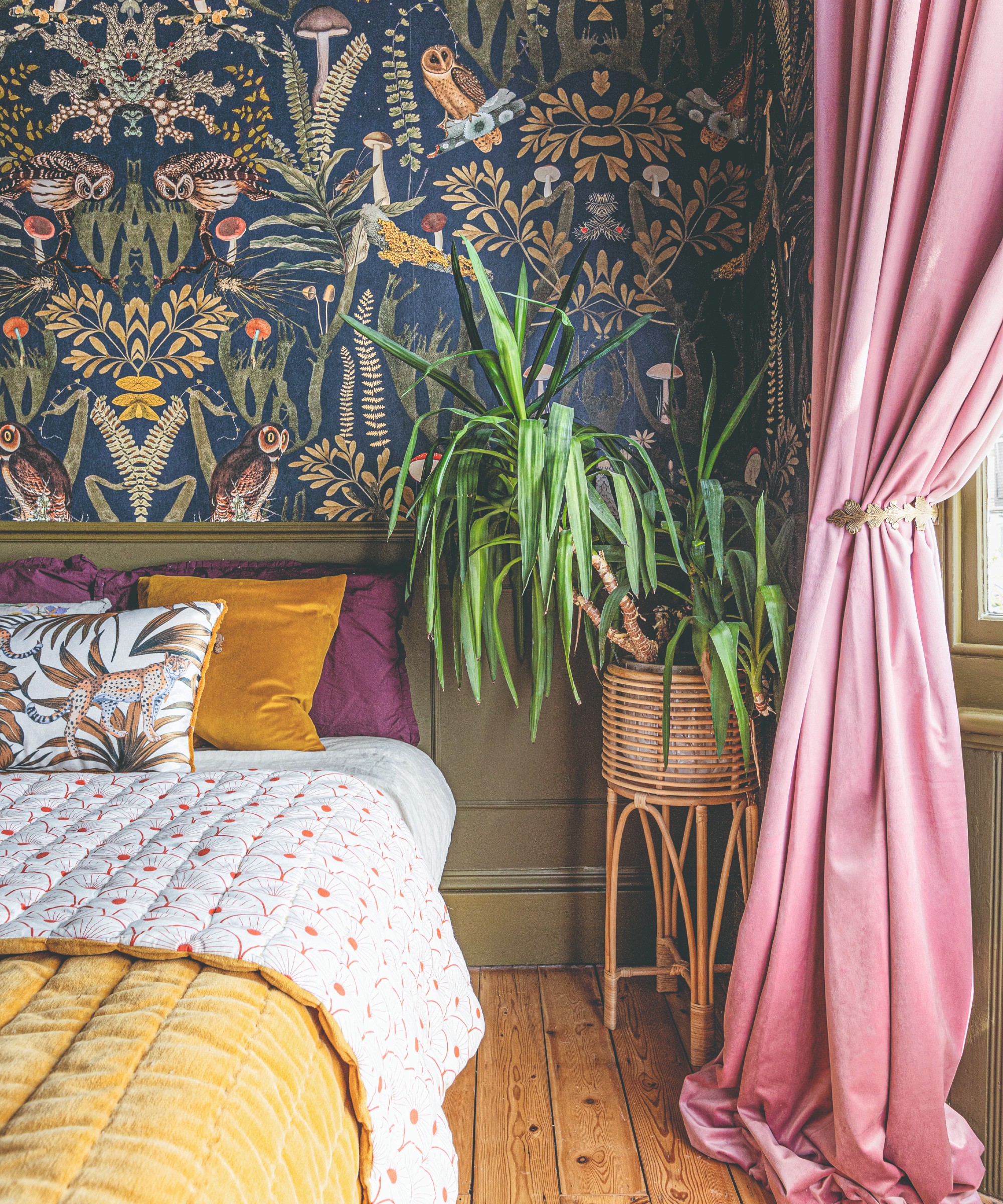 A bedroom with tropical wallpaper on the wall and pink velvet curtain dressing the window