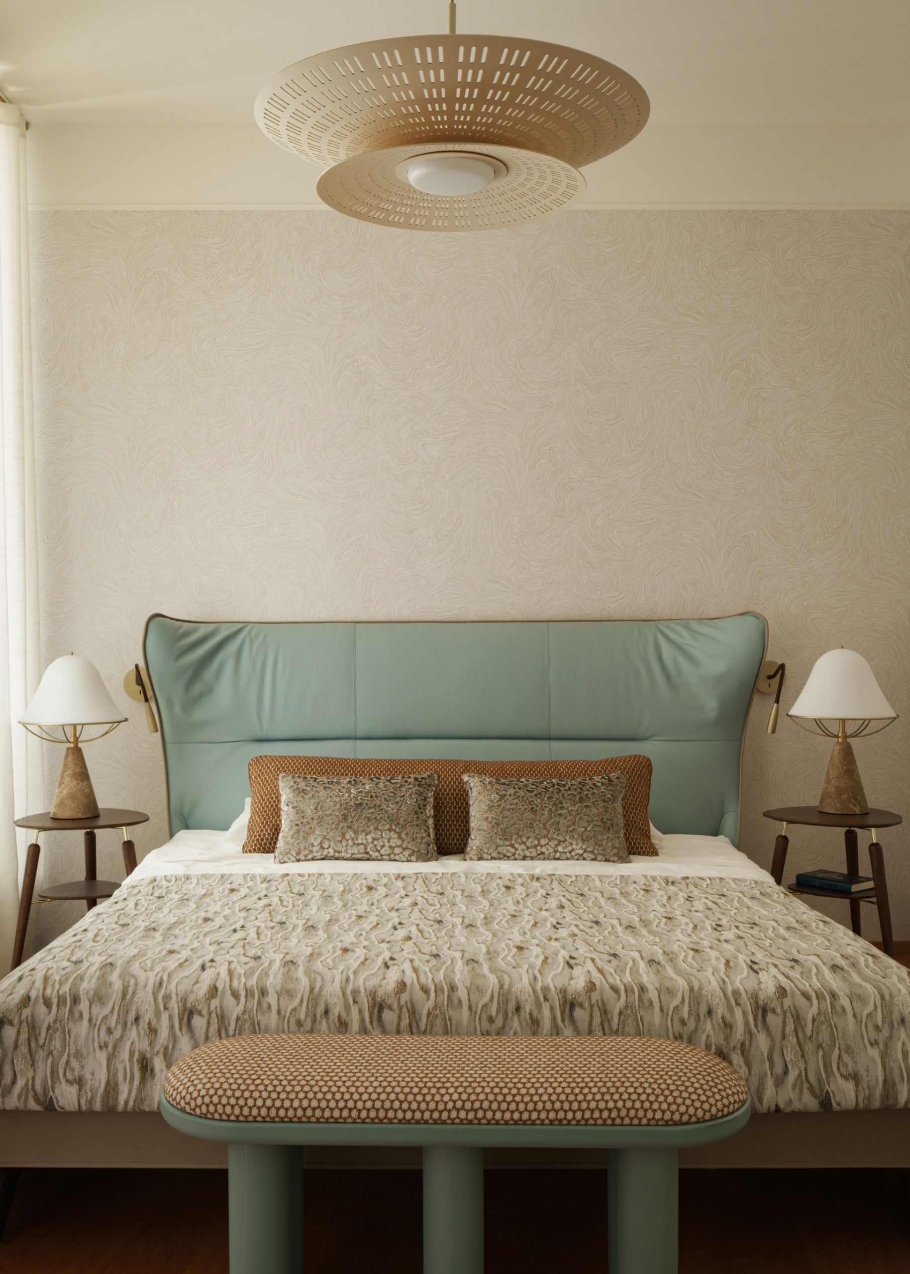 Image of a greige bedroom with a bed that has a large light blue headboard, gray marbled bedding, and orange detailing. There is a pendant light, a lamp, a bench seat and a curtain in the room.