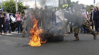 A protester setting fire to an object in San Salvador, El Salvador, in September 2021, with a crowd behind them