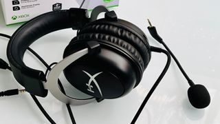 A black gaming headset with a detachable microphone and cushioned ear pads is displayed on a white surface. Xbox branding is partially visible in the background.