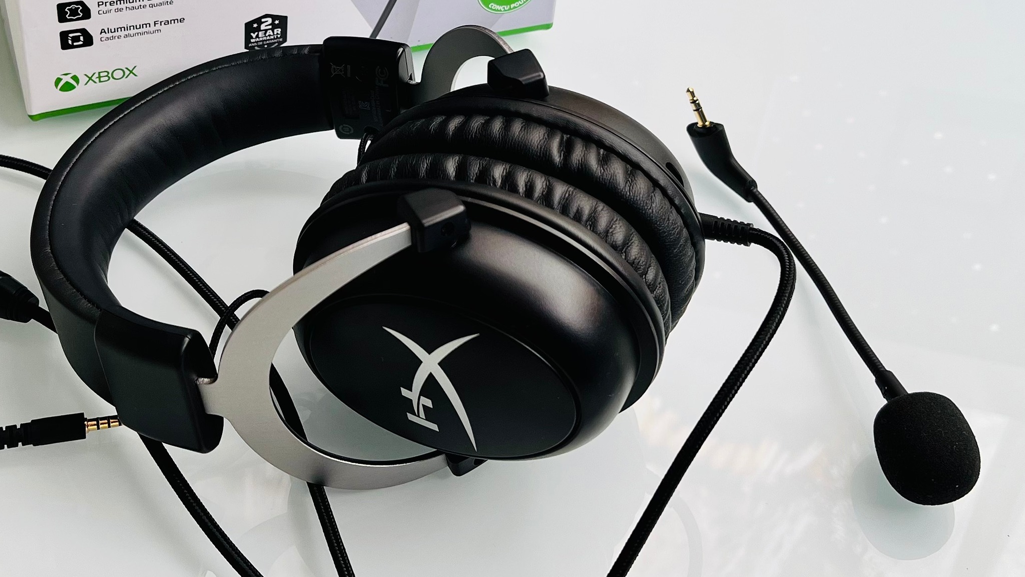 A black gaming headset with a detachable microphone and cushioned ear pads is displayed on a white surface. Xbox branding is partially visible in the background.