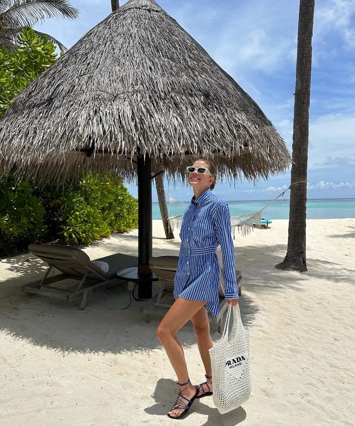 Sofia Grainge wears striped shirt dress, black strappy sandals and crochet Prada bag