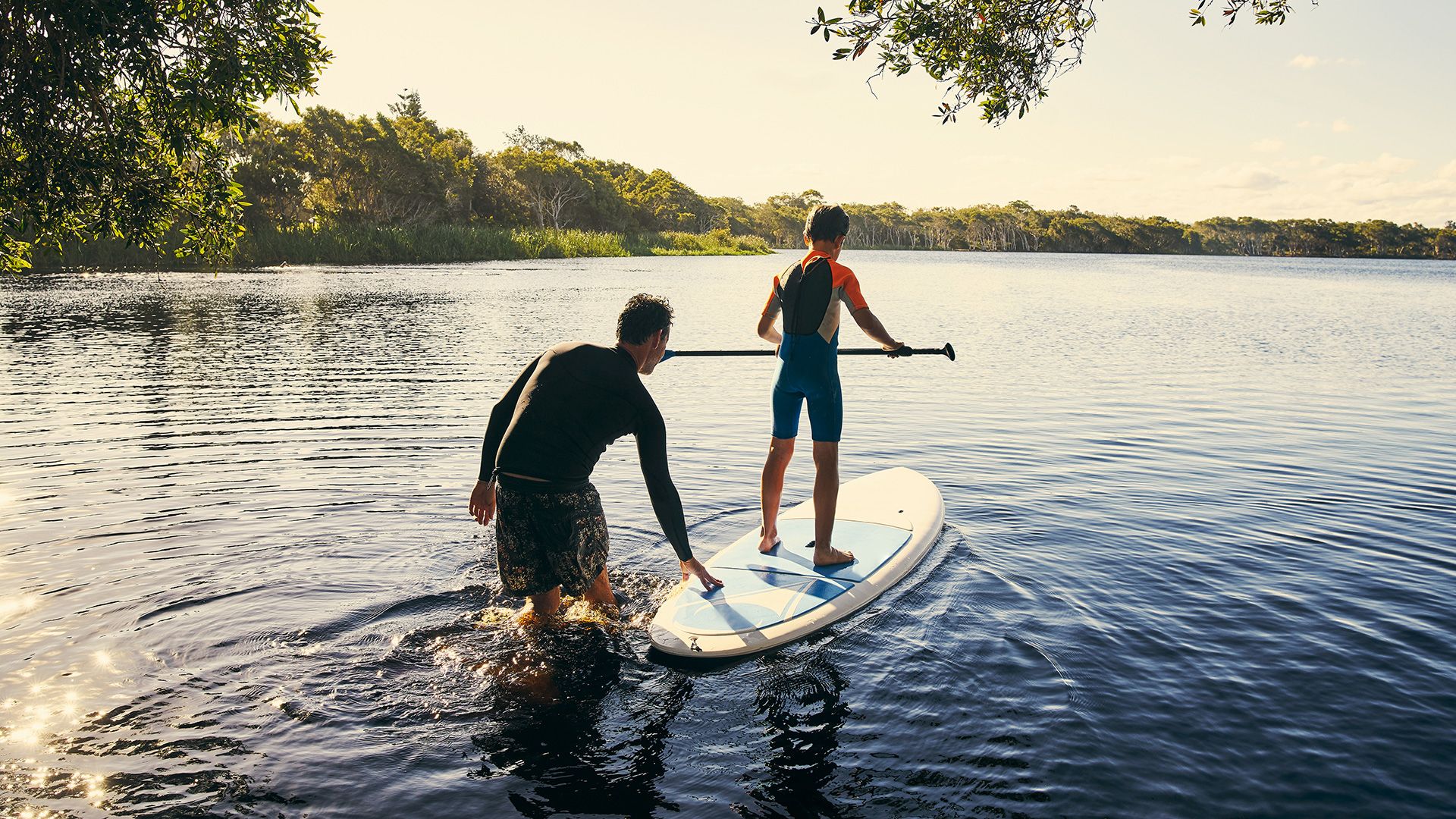 man helping a child onto a paddle board