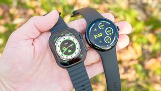 The Apple Watch Ultra 2 next to the Pixel Watch 3 resting in a sun-lit hand with leaves and grass out of focus in the background