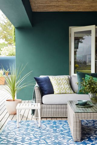 Designing a patio in a teal scheme with decking, blue patterned rug and wicker sofa and coffee table.