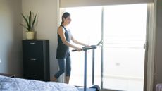 woman in a bedroom walking on a treadmill with french doors behind her 