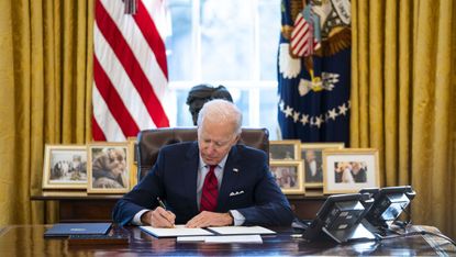 Joe Biden signs an executive order at the Resolute Desk in the Oval Office