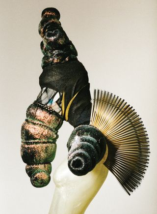 Side view of bee sculpture made from wigs, spray paint, glitter and chopsticks, white background