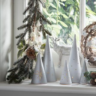 Silver cone Christmas tea lights on windowsill with foliage garland and stag decoration