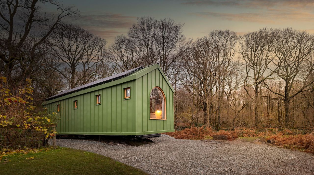 The outside of the green caravan with the lights on seen amongst woodland