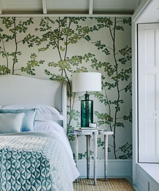 A bedroom with green-blue bed linen and a mural-like wallpaper covered in trees
